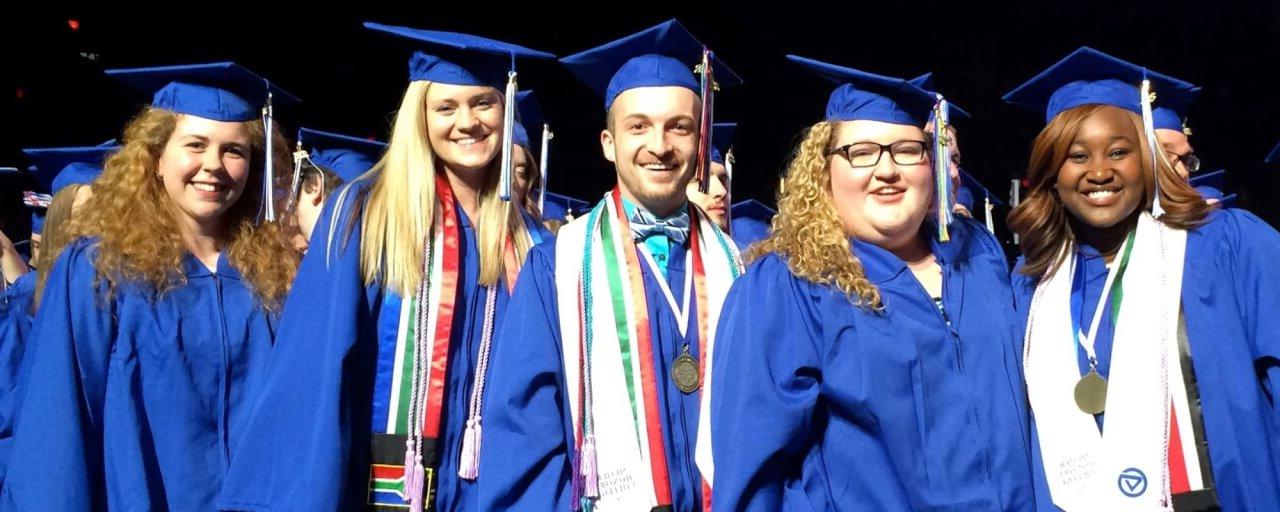 Five students wearing graduation caps and gowns, smiling